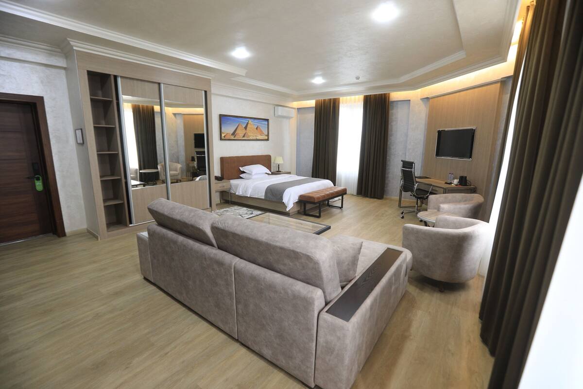 Une chambre d’hôtel comprenant un lit, un canapé, un fauteuil, un bureau et un téléviseur.