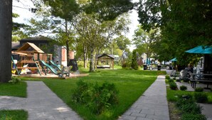 Ein Spielplatz mit Rutschen und einer Holzkonstruktion, umgeben von einem gepflegten Rasen und Bäumen.