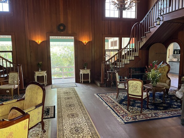 A spacious interior with a wooden staircase, multiple seating areas, and a view through a large door to the outdoors.