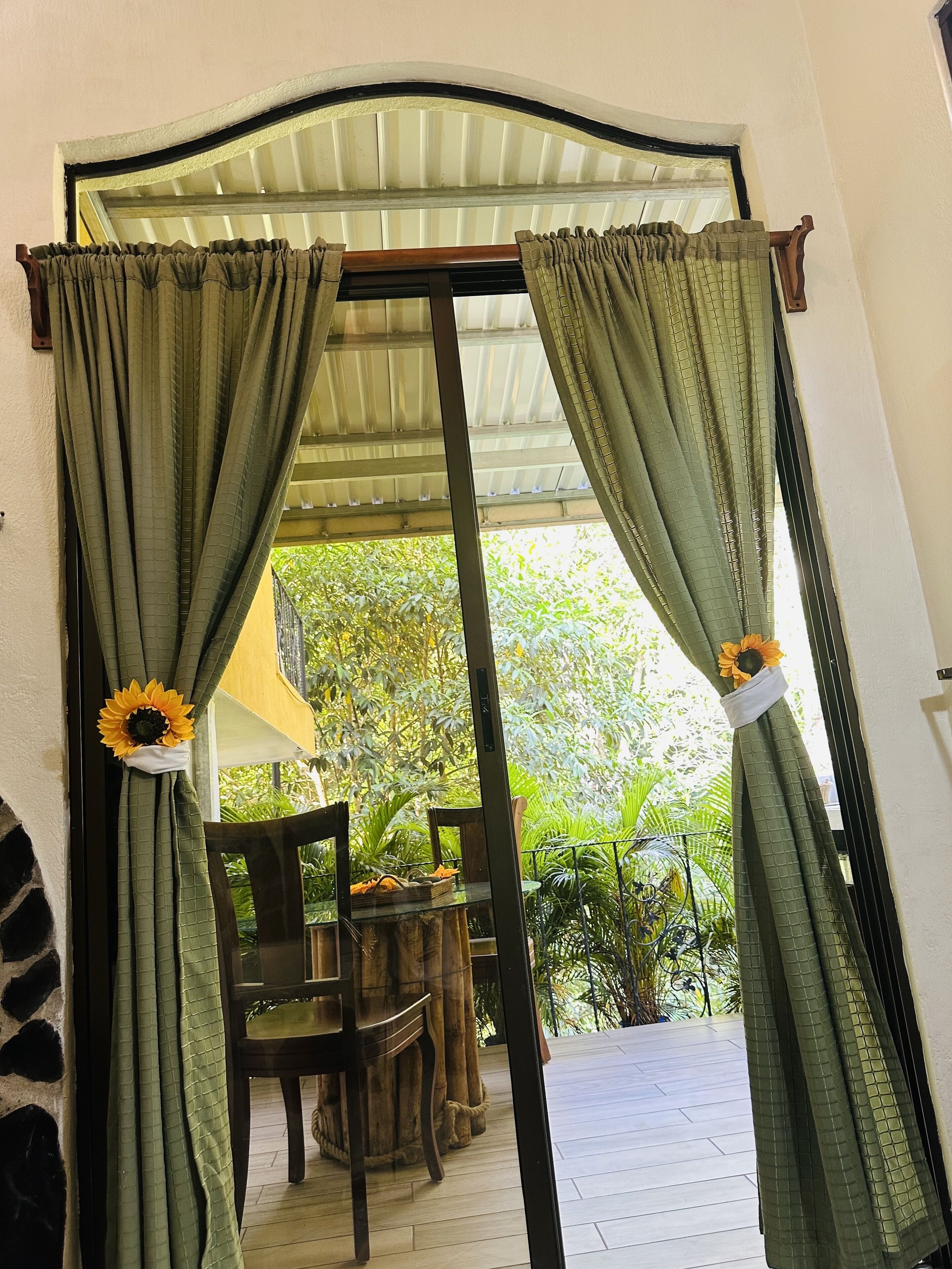 A doorway with green curtains and sunflowers, leading to an outdoor area with a table and chairs.