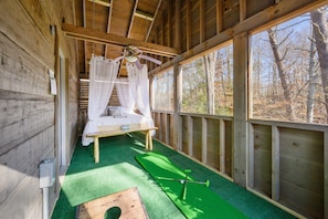 A wooden cabin with a bed, a ceiling fan, and a view of the forest.