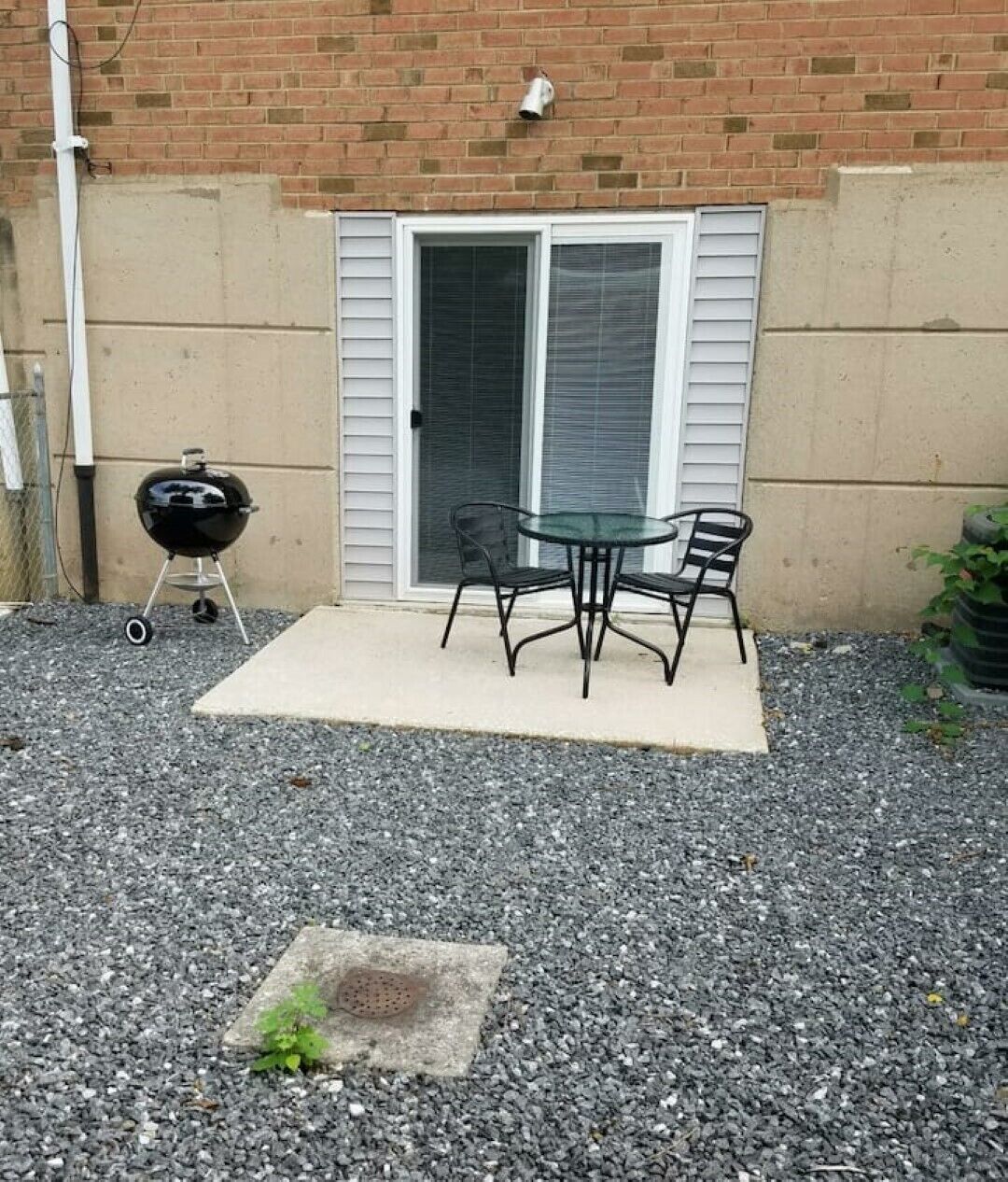 A patio with a table and chairs, a grill, and a door with shutters.