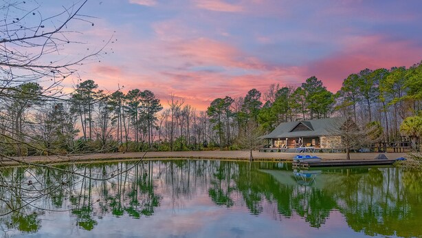 A lakeside cabin with a dock and a boat, surrounded by trees and a clear sky. - Secluded Lodge 8acres Hot Tub, Pingpong kayaks! (Sampson County)