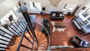 A spacious living room with a spiral staircase, leather furniture, and a large window. - Secluded Lodge 8acres Hot Tub, Pingpong kayaks! (Sampson County)