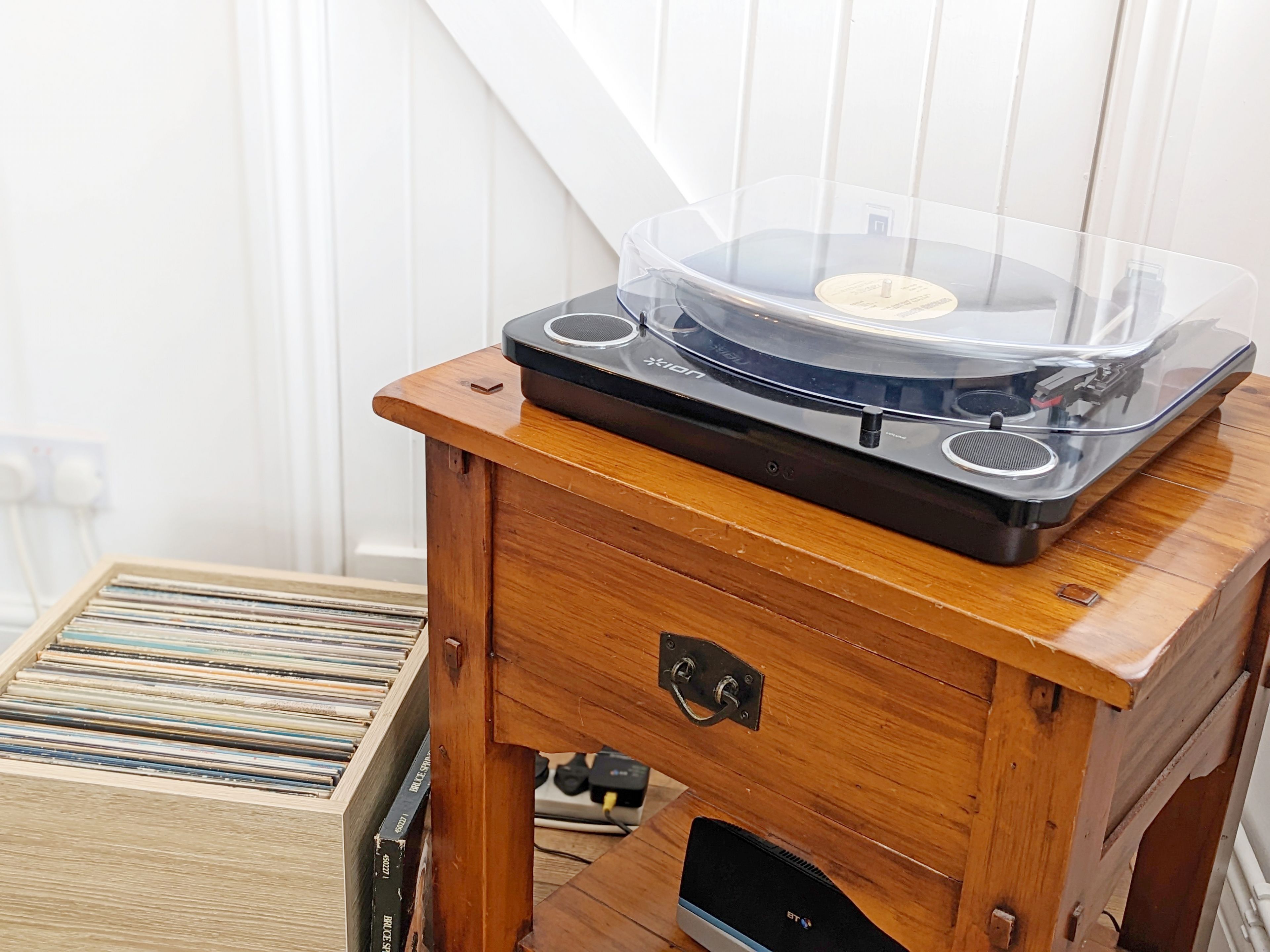 Un reproductor de música de madera con una cubierta transparente y un disco encima, sobre una mesa de madera.