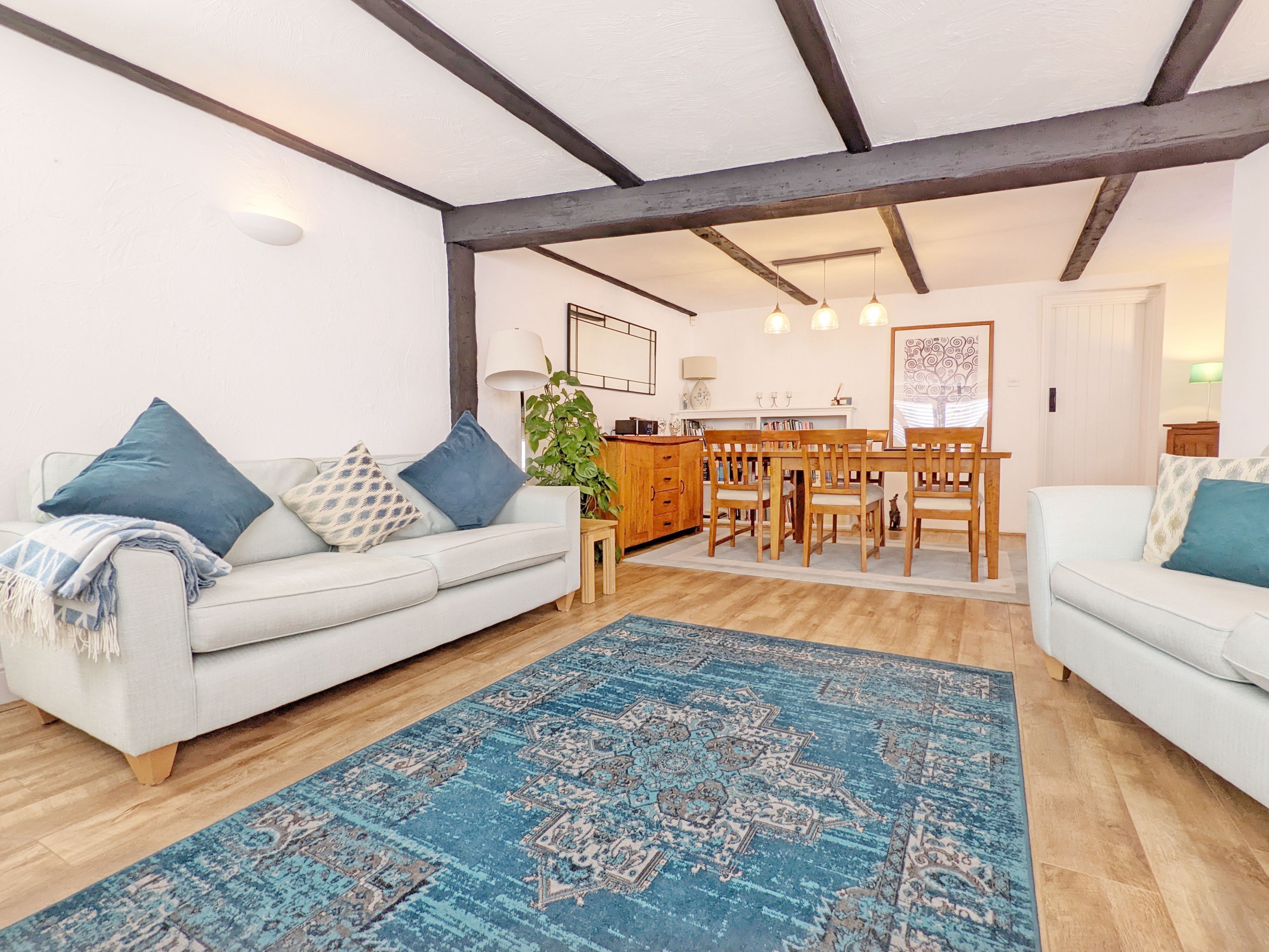A spacious living room with a light-colored sofa, a blue patterned rug, and a wooden dining table with chairs.
