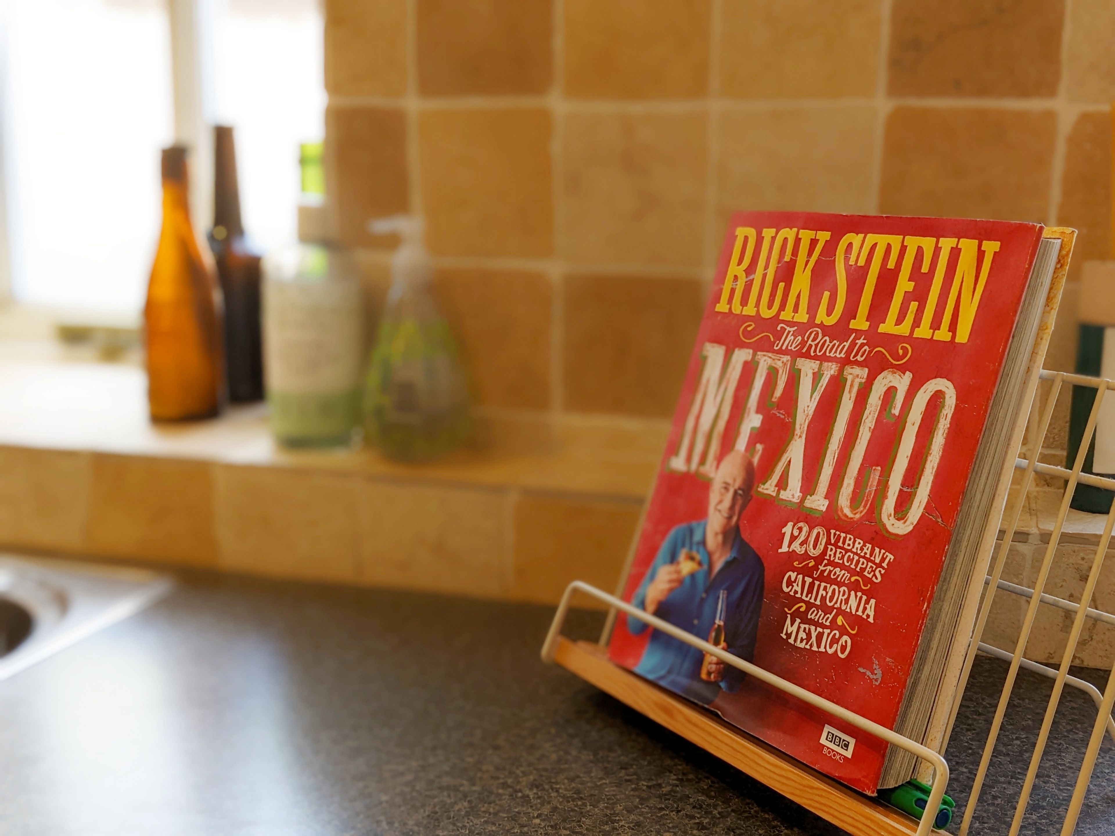 A kitchen counter with a rack holding a book titled 'Rick Steinfeld: The Road to Mexico'.