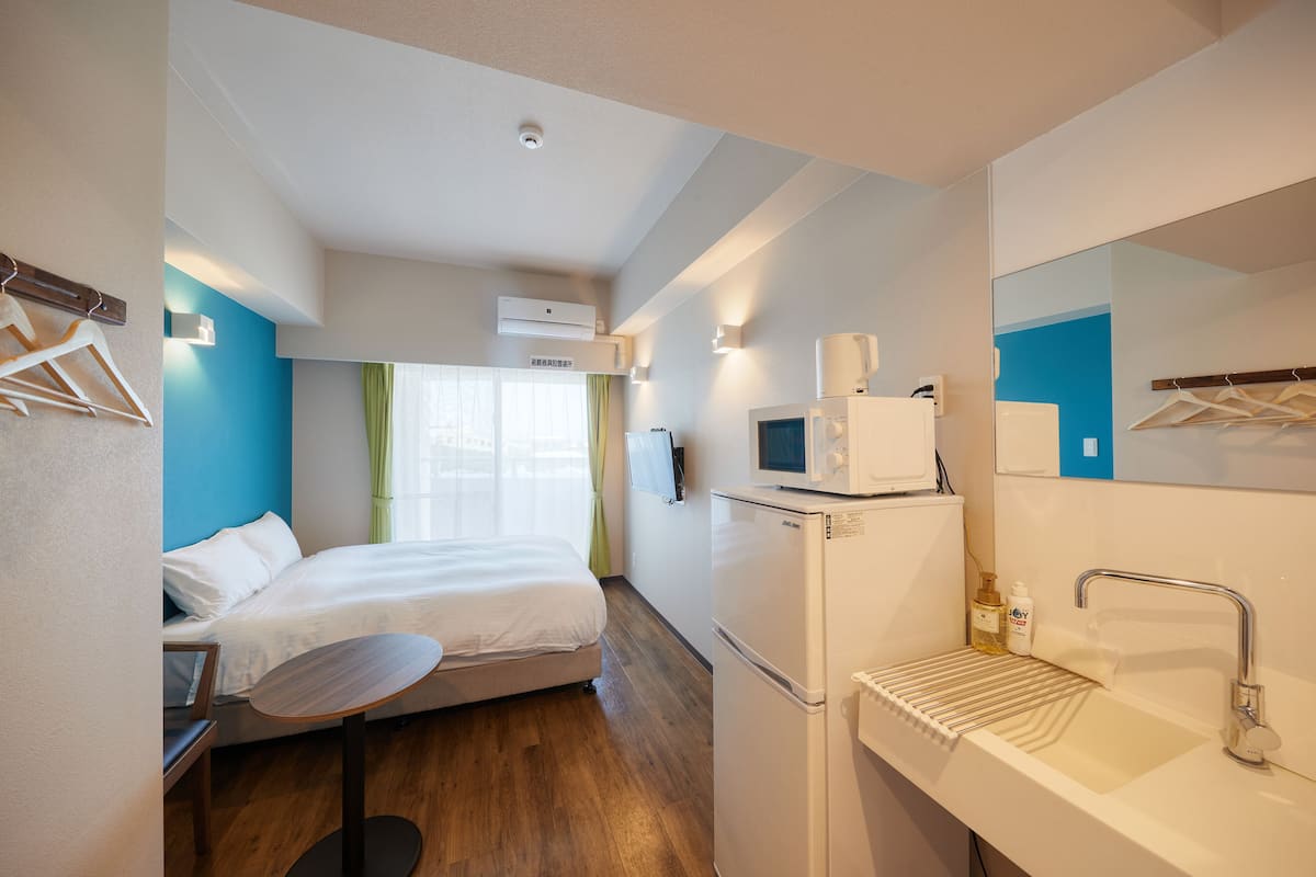 A hotel room with a bed, a small table, a sink, and a microwave.