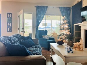 Uma sala de estar com sofá, uma poltrona, uma mesinha de centro com uma árvore de Natal e lareira.