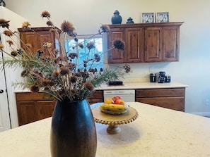 Uma cozinha com armários de madeira, um vaso com flores secas e uma tigela de frutas no balcão.