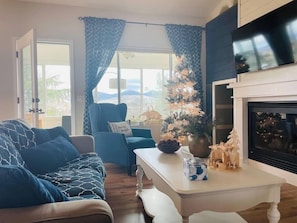 Uma sala de estar com sofá, poltrona, mesa de centro, lareira e árvore de Natal.