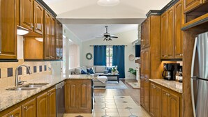 Cozinha com armários de madeira, geladeira de aço inoxidável e área de jantar com sofá e mesa de centro.