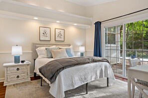 A bedroom with a bed, nightstands, and a view through a large window.