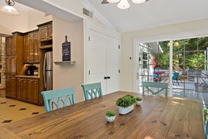 A kitchen with wooden cabinets, a stainless steel refrigerator, and a dining table with chairs. There are potted plants on the table.