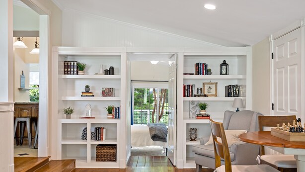 Uma sala de estar aconchegante com piso de madeira, uma mesa de jantar e uma estante repleta de livros e objetos decorativos.