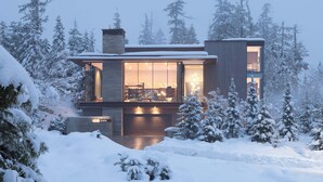 A modern house with a large garage, surrounded by snow-covered trees. - Kadenwood estate with heated pool & hot tub (Whistler)