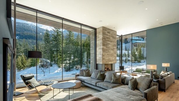 A modern living room with a large window, a fireplace, and a sofa. - Kadenwood estate with heated pool & hot tub (Whistler)