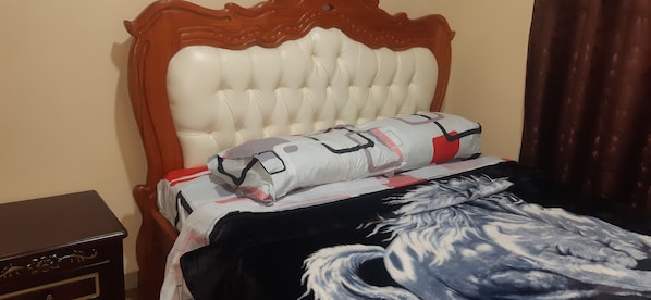 Una cama con cabecera tapizada de blanco, manta estampada y almohada con diseño deportivo.