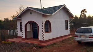 A small, single-story building with a sloped roof, a front entrance with an arched doorway, and two windows with arched tops. - Lena Cottage - 10km from Nanyuki Town towards Timau (Nanyuki)