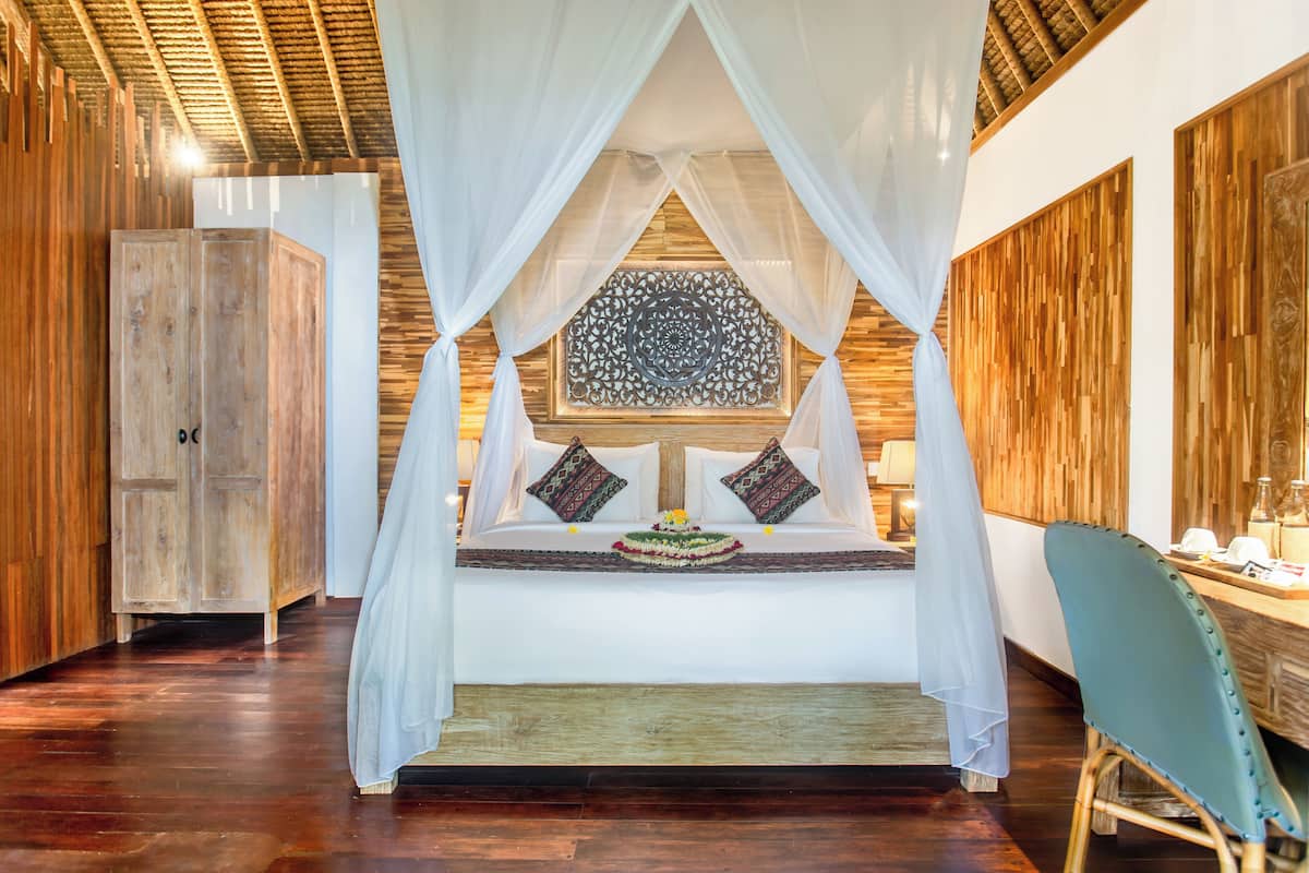 A room with a bed under a canopy, a wooden wardrobe, and a chair.