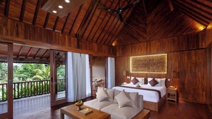 A spacious room with a large bed, a sofa, a wooden coffee table, and a balcony with a view of lush greenery. - Manah Shanti Suites by GenuineHost (Ubud)