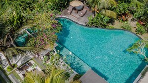 An aerial view of a swimming pool surrounded by lush greenery and a wooden deck with lounge chairs and an umbrella. - Manah Shanti Suites by GenuineHost (Ubud)
