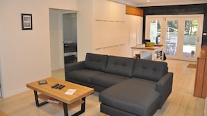 Een moderne woonkamer met een hoekbank, een houten salontafel en een keuken die zichtbaar is door een open deur.