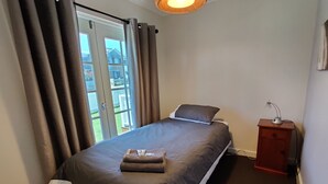Een slaapkamer met een bed, nachtkastje, lamp en uitzicht.