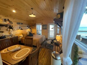 A cozy cabin with a wooden interior, a dining area, a bed, and a balcony with a view.