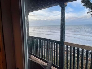 A view from a balcony overlooking a calm sea with a wooden deck and metal railing.