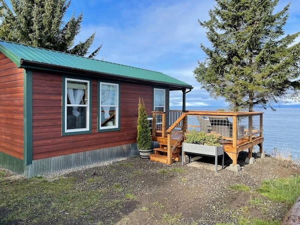 A wooden cabin with a green roof, a deck, and a view of the water.