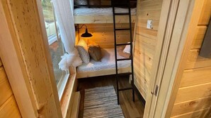 Una cama individual superpuesta con escalera, una ventana con cortinas y una alfombra pequeña en el suelo.