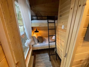 A bunk bed with a ladder, a window with curtains, and a small rug on the floor.