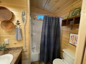 A wooden cabin bathroom with a shower, a toilet, a sink, and a shelf with decorative items.
