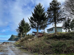 A coastal property with a house on a hillside, a rocky beach, and a view of the ocean.
