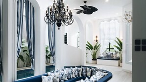 A modern living room with a blue sofa, patterned cushions, a chandelier, and large windows with curtains. - OriVista Stylish 3BR Villa Muzo in Seminyak, Pool, Wifi, Beach (Seminyak)
