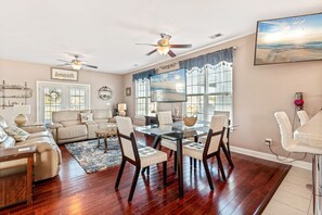 A spacious living room with a glass dining table, leather sofas, and a ceiling fan. - Waterfront Home with Multiple Decks, Central AC, WiFi, and Outdoor Shower (North Myrtle Beach)