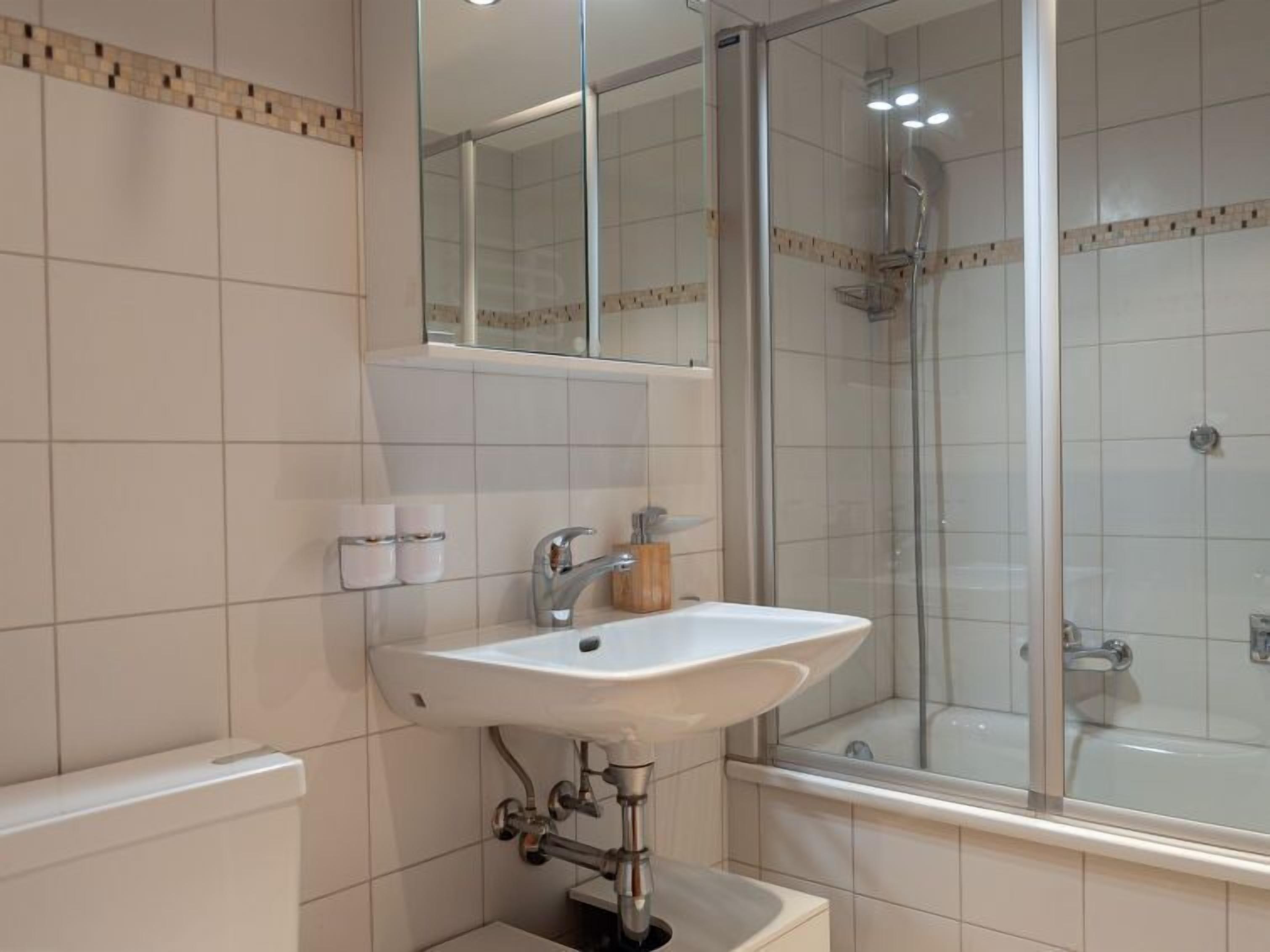 Un bany amb un lavabo blanc, un mirall i una dutxa amb portes de vidre.
