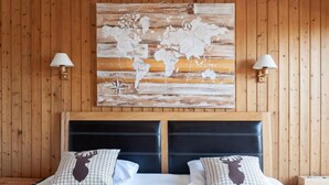 Une chambre d’hôtel avec un mur lambrissé en bois, une grande œuvre d’art représentant une carte du monde, une tête de lit noire et deux coussins à carreaux ornés d’un motif d’élan.