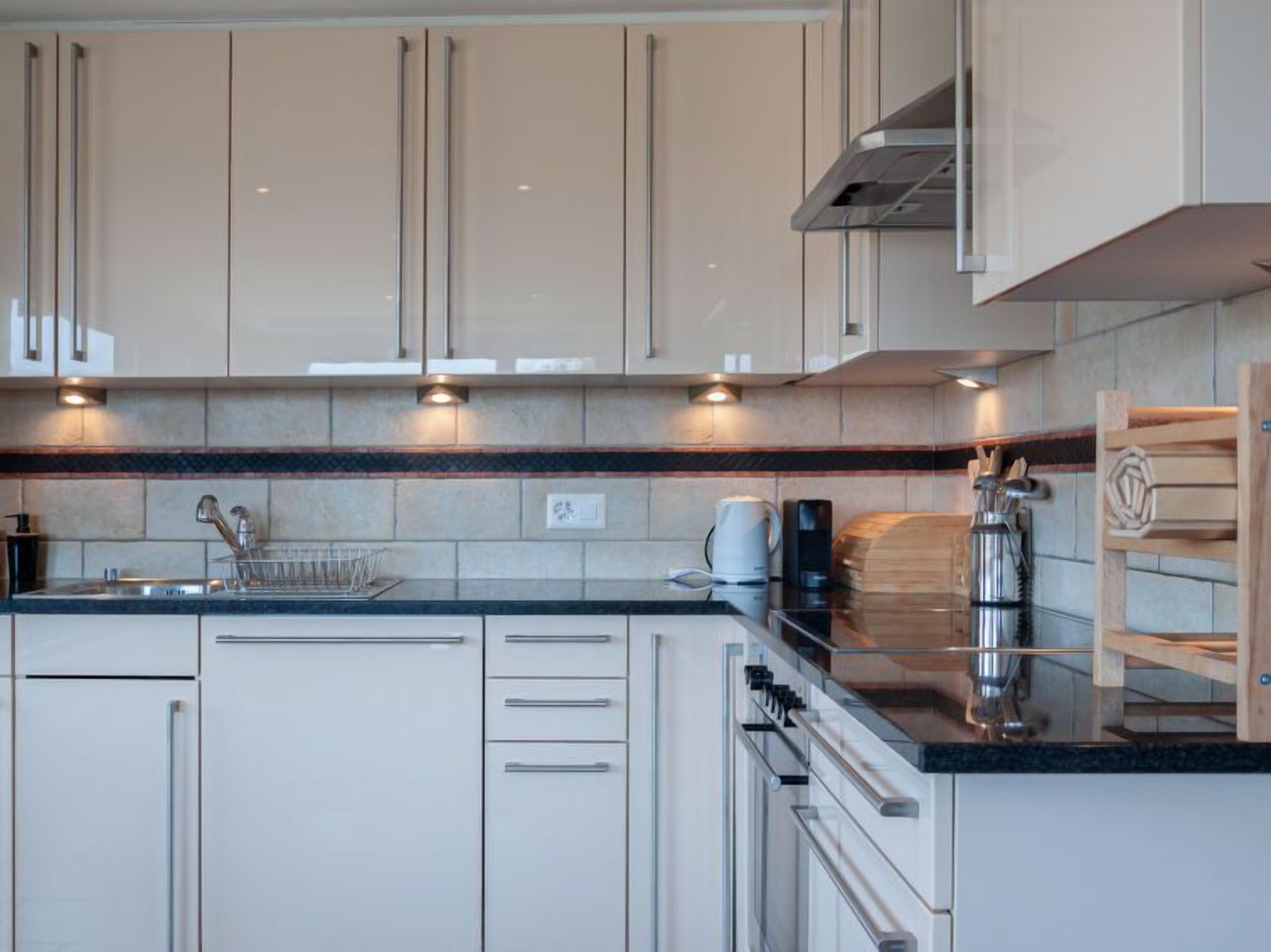 Een moderne keuken met witte kasten, een zwart aanrecht en roestvrijstalen apparatuur.