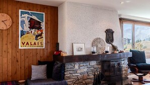 Une pièce chaleureuse avec un mur en bois, une cheminée en pierre, une horloge murale et une vue magnifique par la fenêtre.