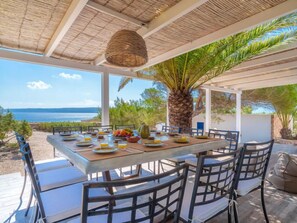 Un espace de restauration en plein air avec une table dressée pour le petit-déjeuner, offrant une vue panoramique sur la mer et les montagnes.