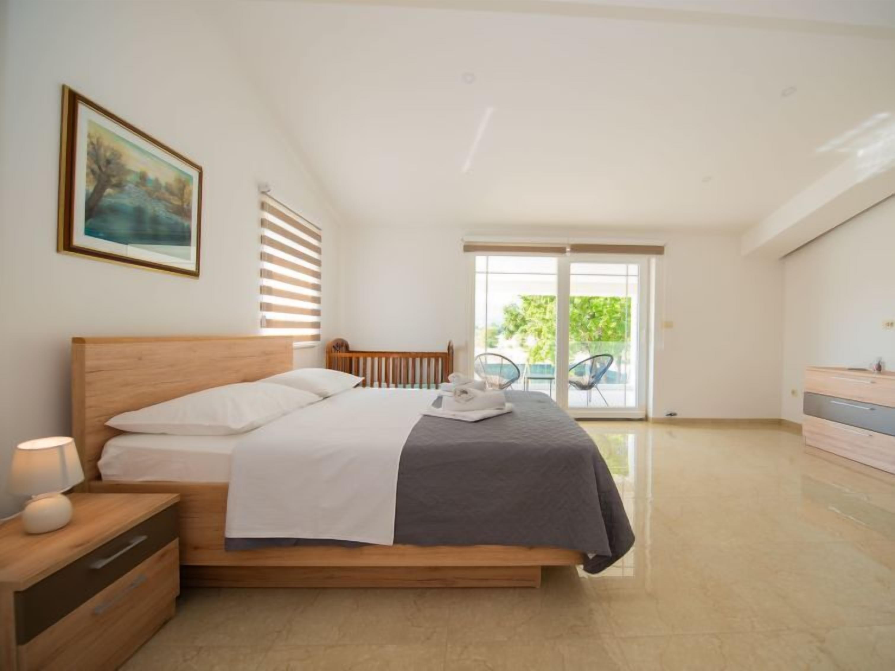 Une chambre avec un lit en bois, une table de chevet, une commode et un balcon avec des chaises.
