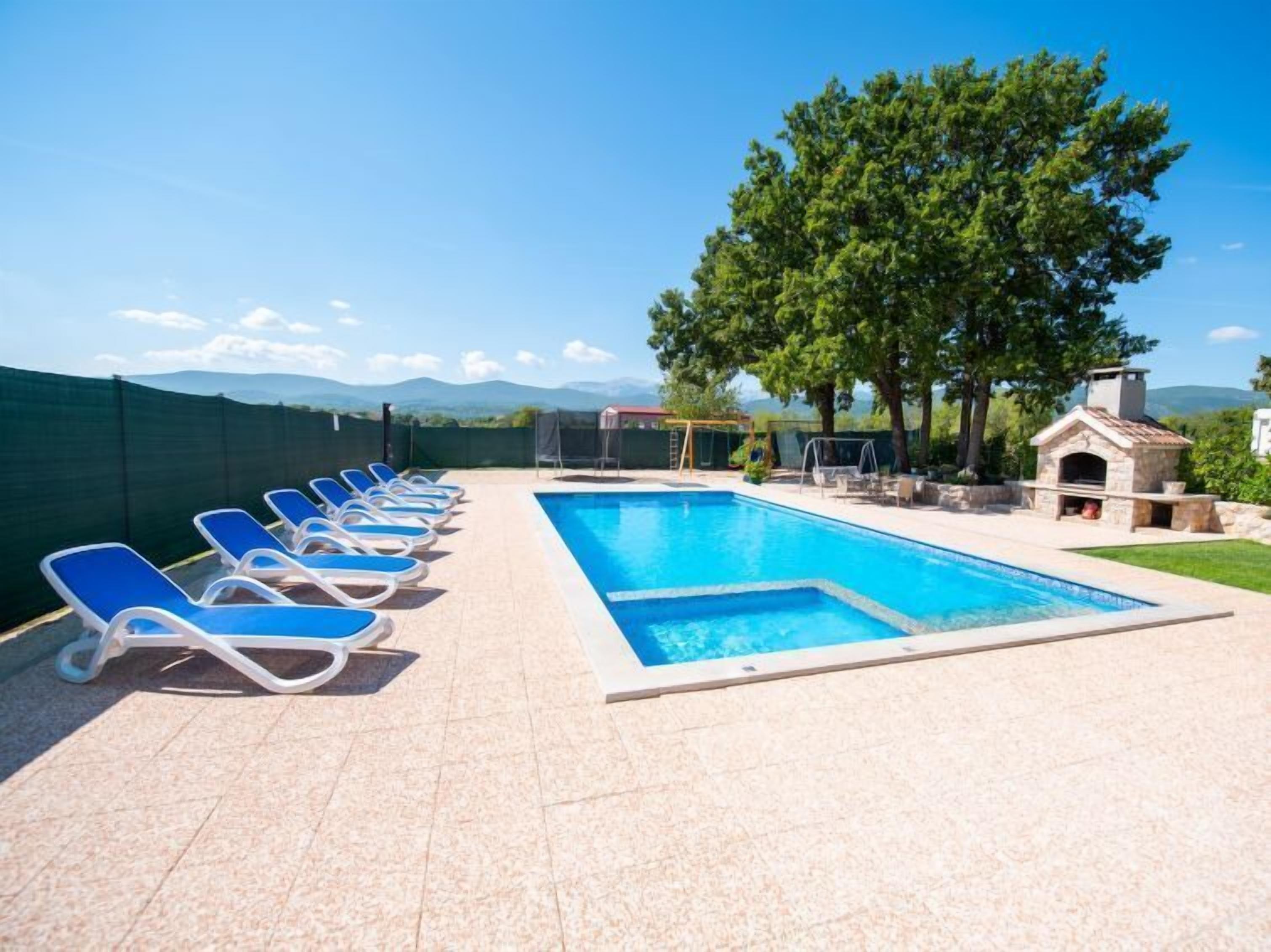 A swimming pool with lounge chairs, a small outdoor kitchen, and a view of mountains.