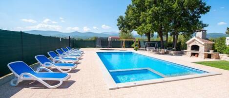 A swimming pool with lounge chairs, a small outdoor kitchen, and a view of mountains.