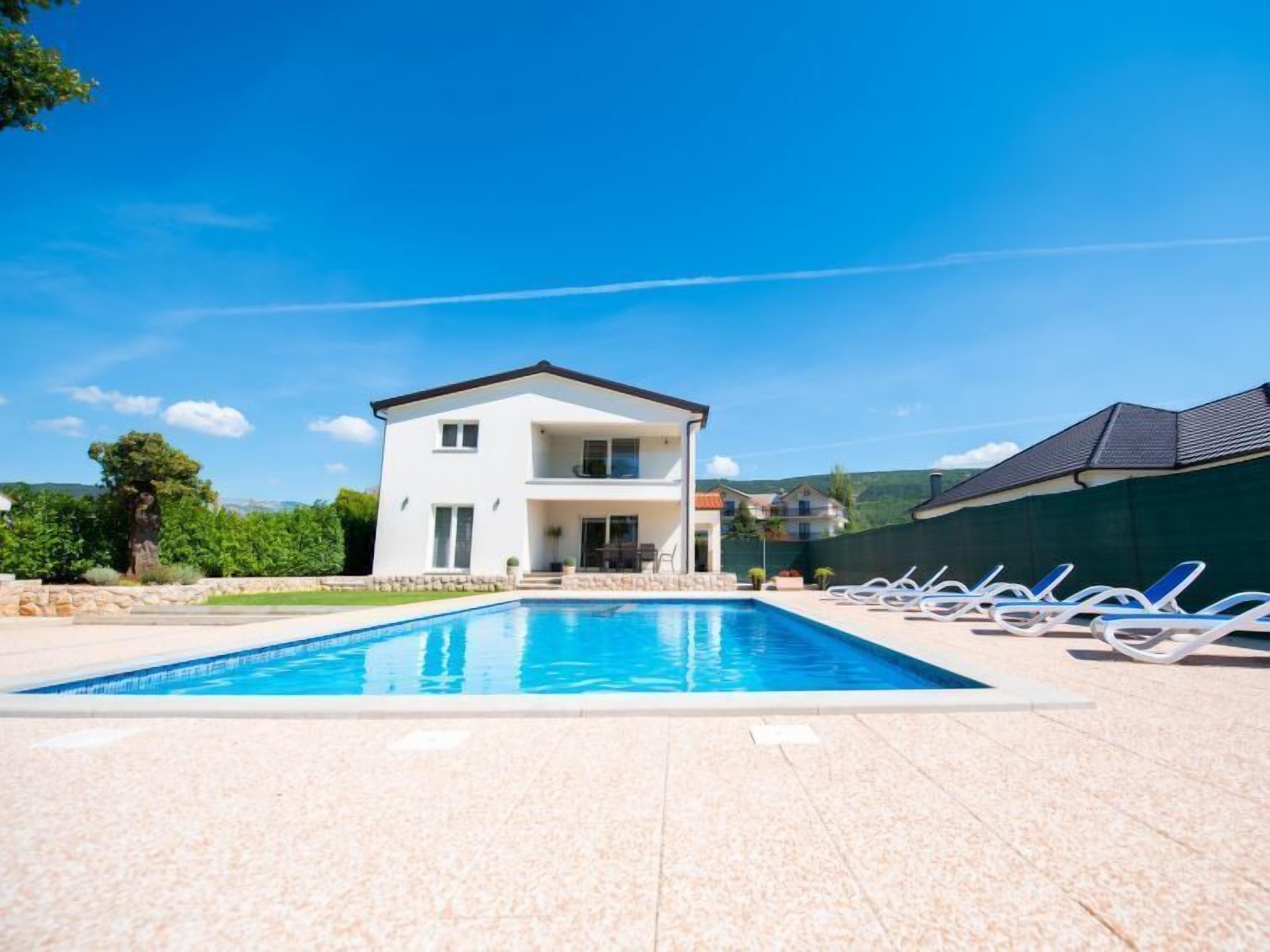 Uma casa de dois andares com piscina e cadeiras de descanso.