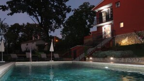 Una piscina con agua cristalina, rodeada de sillas de descanso y sombrillas, y un edificio rojo con fachada de piedra al fondo.