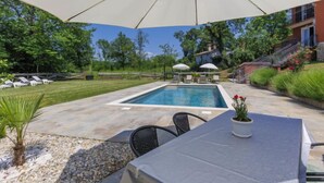 Terraza junto a la piscina con mesa, sillas y sombrillas.