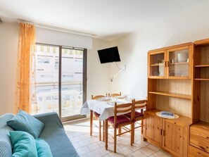 Quarto com sofá, mesa de jantar com cadeiras, televisão na parede e armário de madeira com portas de vidro.
