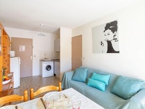 Um espaço compacto com cozinha compacta, máquina de lavar, sala de jantar com mesa posta para dois e sofá azul claro.